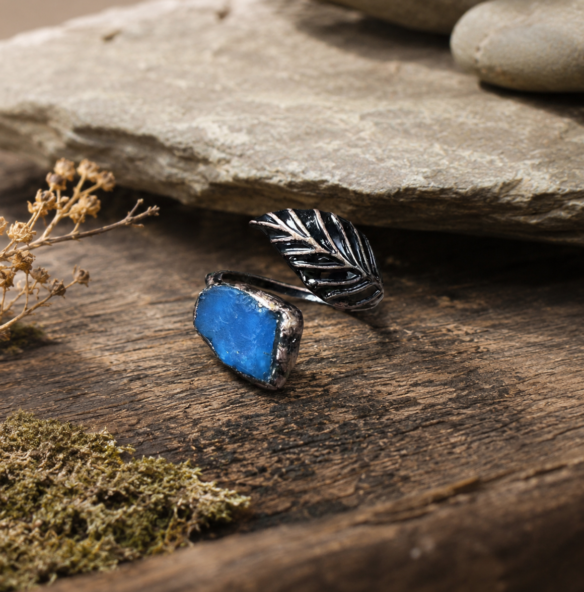 Blue apatite feather ring with lake-blue gemstone, dark feather detail, and rustic natural setting.