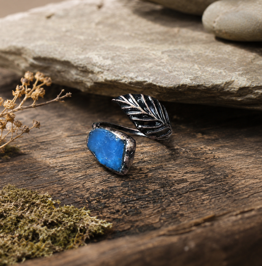 Blue apatite feather ring with lake-blue gemstone, dark feather detail, and rustic natural setting.