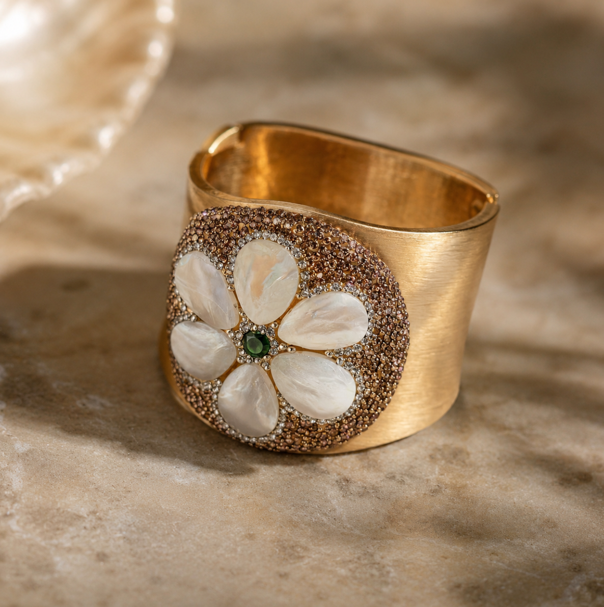 Pearl shell bracelet with mother-of-pearl flower petals, green gemstone center, and wide gold cuff design.
