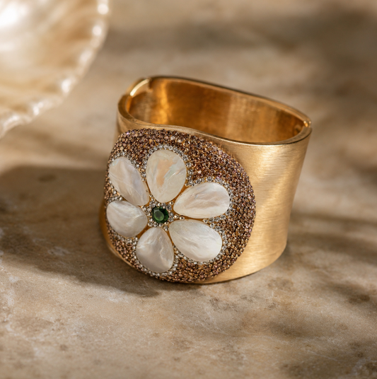 Pearl shell bracelet with mother-of-pearl flower petals, green gemstone center, and wide gold cuff design.