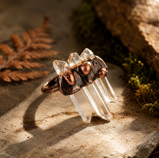 Clear quartz ring with three transparent crystal points, copper-tone setting, and warm forest sunlight.