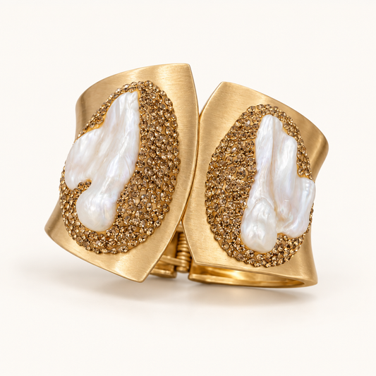 Gold-tone pearl bracelet with two irregular white baroque pearls in a wide cuff on an off-white background