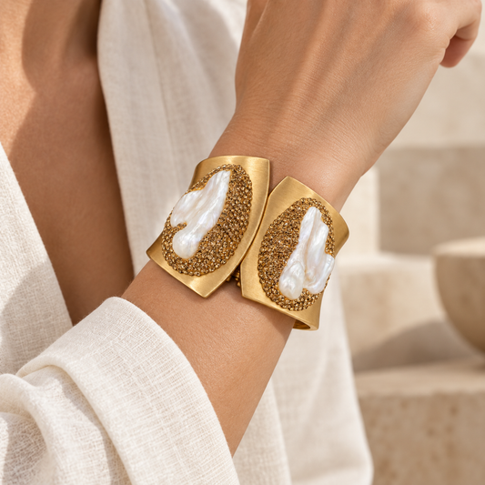 Woman wearing a gold-tone pearl bracelet in a wide cuff bracelet style, showing its scale and paired white pearls