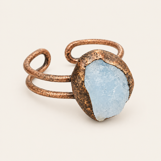 Raw pale-blue aquamarine ring on warm off-white, showing the irregular stone outline and split-band structure.