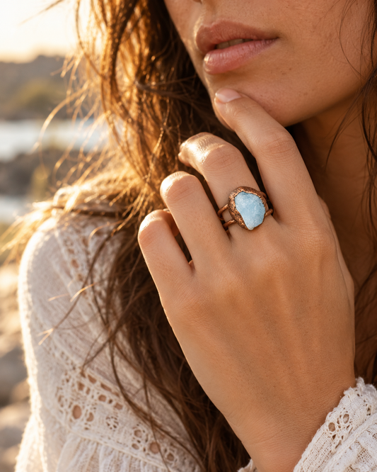 Aquamarine ring worn on the hand near the face, showing the pale-blue raw stone at real scale and its visual presence.