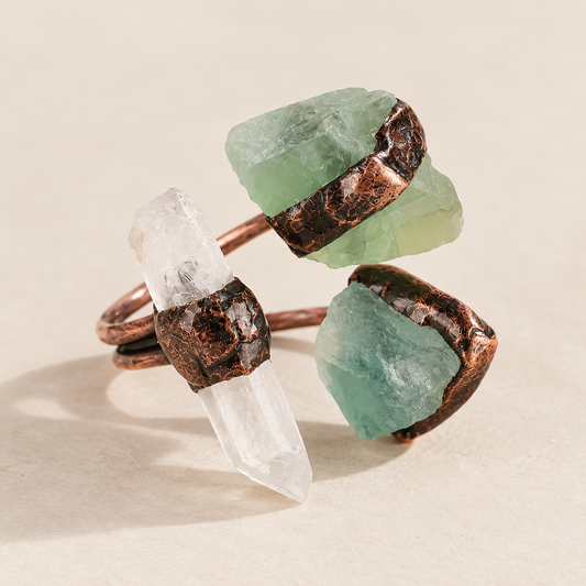 Clear quartz and green fluorite three stone ring on warm off-white, showing its open band and raw stone shapes.