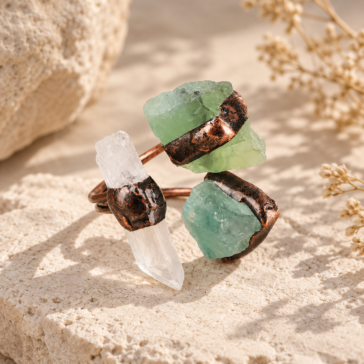 Three stone ring on natural stone in warm light, showing clear quartz, green fluorite, and its open sculptural profile.