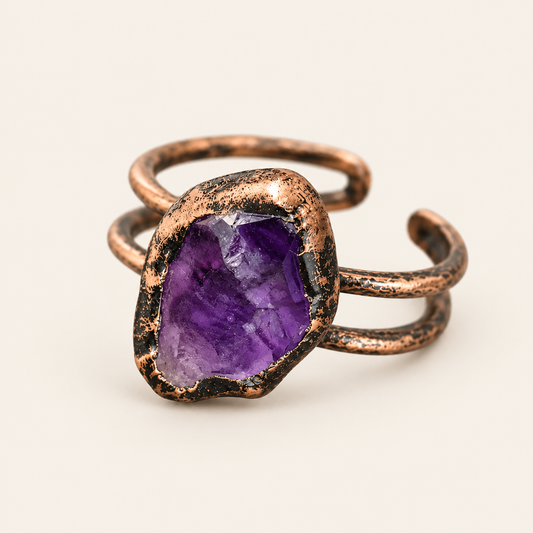 Raw purple amethyst ring on warm off-white, showing the irregular stone, dark-toned border, and open double-band form.