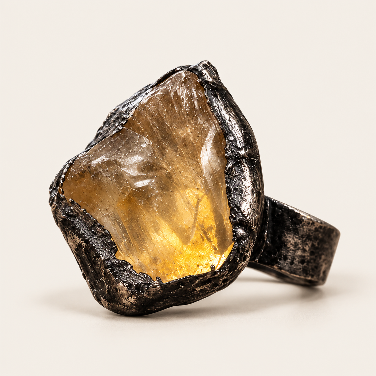 Raw honey-yellow citrine ring on warm off-white, showing the irregular stone and dark-toned sculptural setting.