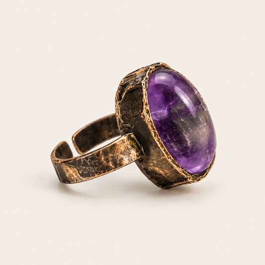 Polished oval amethyst ring on warm off-white, showing the violet stone, domed profile, and dark-toned setting.