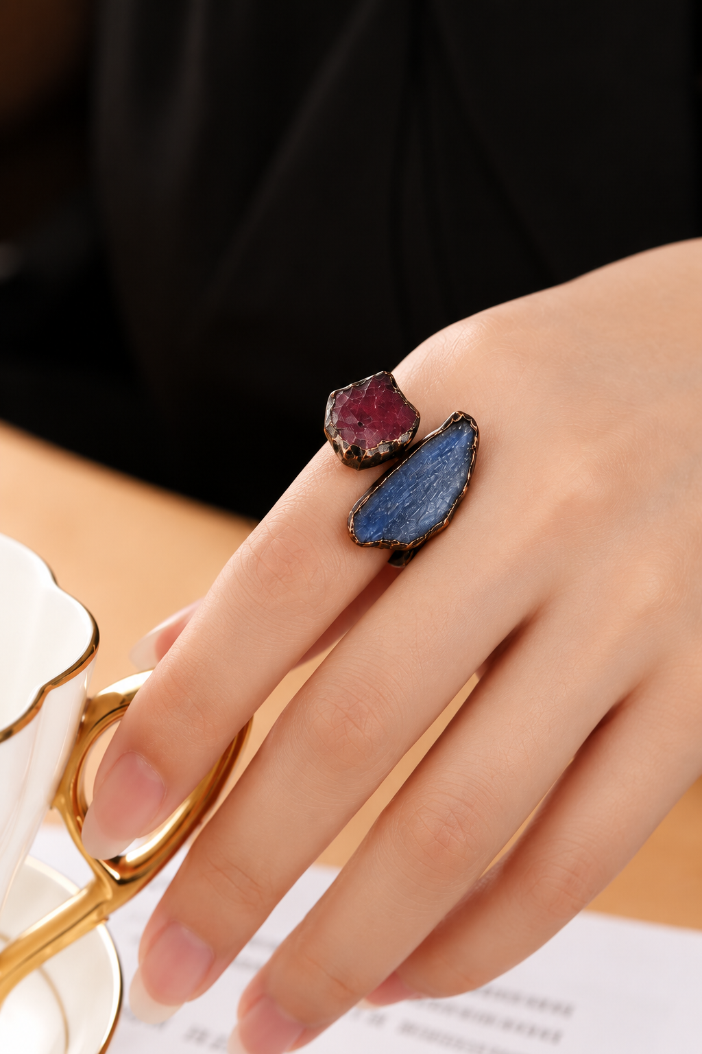 Red stone and blue kyanite ring worn on a hand, showing the contrasting colors and elongated blue stone.