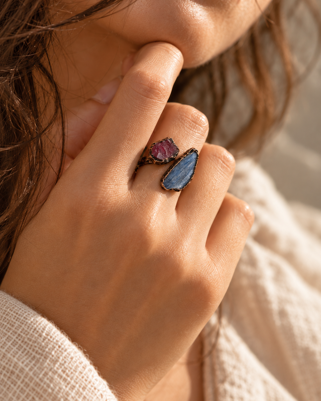 Close-up of a red stone and blue kyanite ring worn on a finger, showing irregular outlines and visible surface textures.