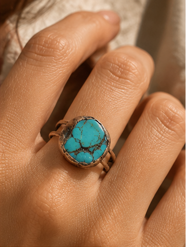 Close-up of a turquoise ring worn on the finger, showing natural dark matrix lines and irregular stone edges.