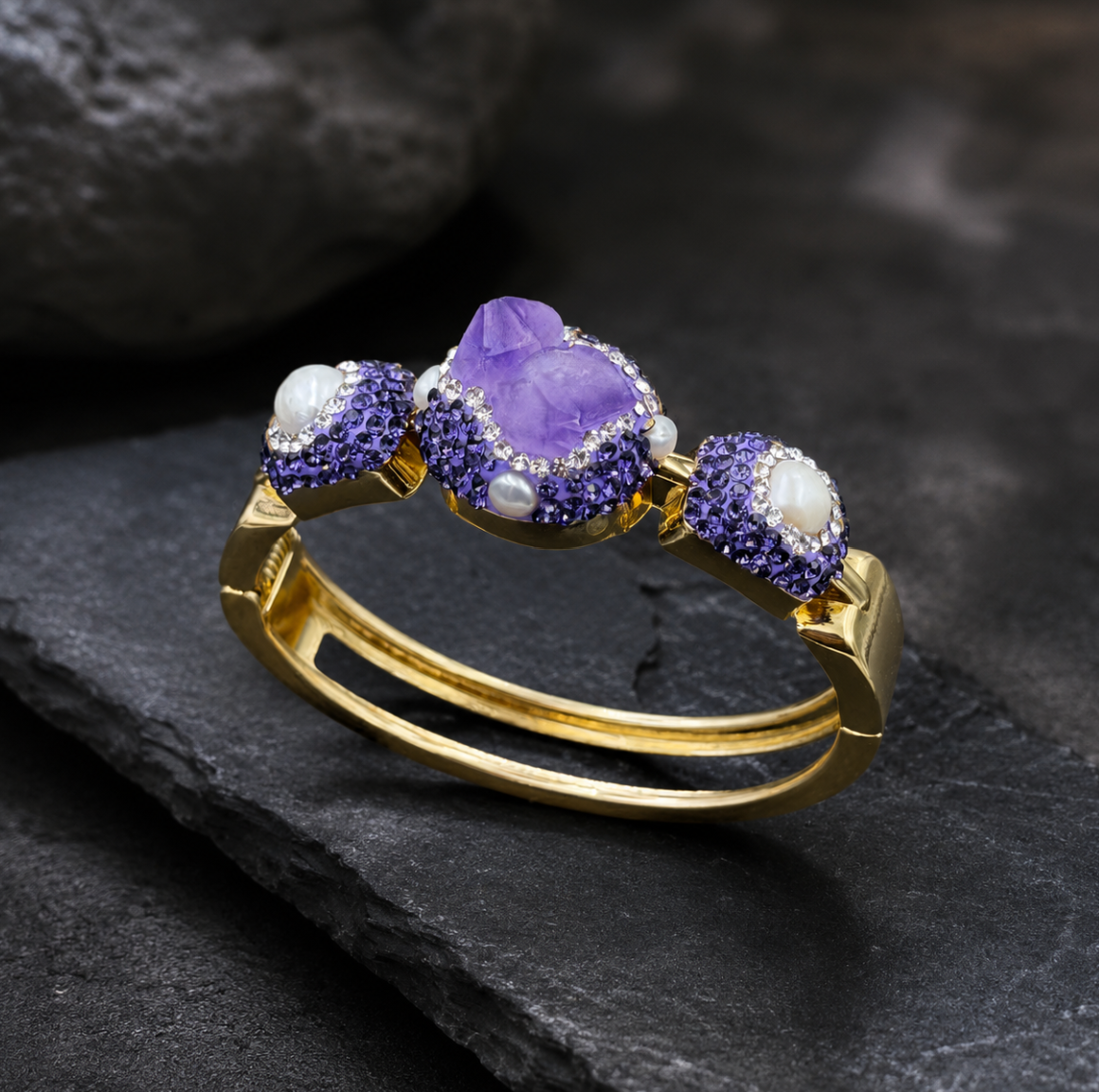 Elegant amethyst cuff bracelet styled on dark stone with raw amethyst, soft pearls, and sculptural gold lines.