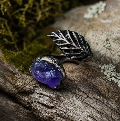Amethyst ring with feather shaped ring design, dark metal texture, and quiet mystical gemstone mood.