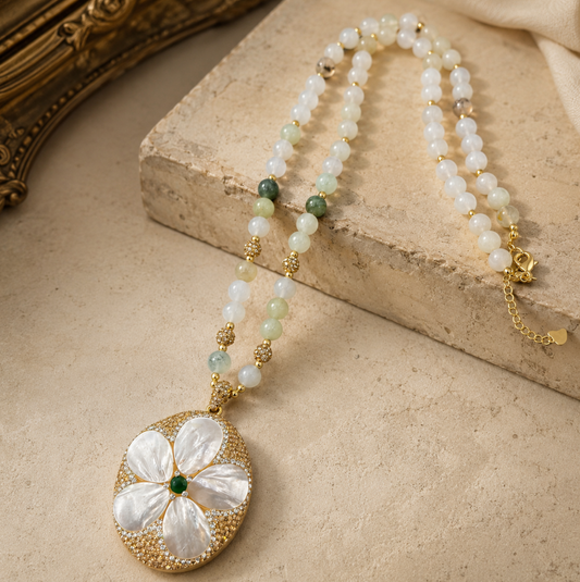 Pearl shell necklace with floral mother-of-pearl pendant, soft pearl beads, and green gemstone accent.