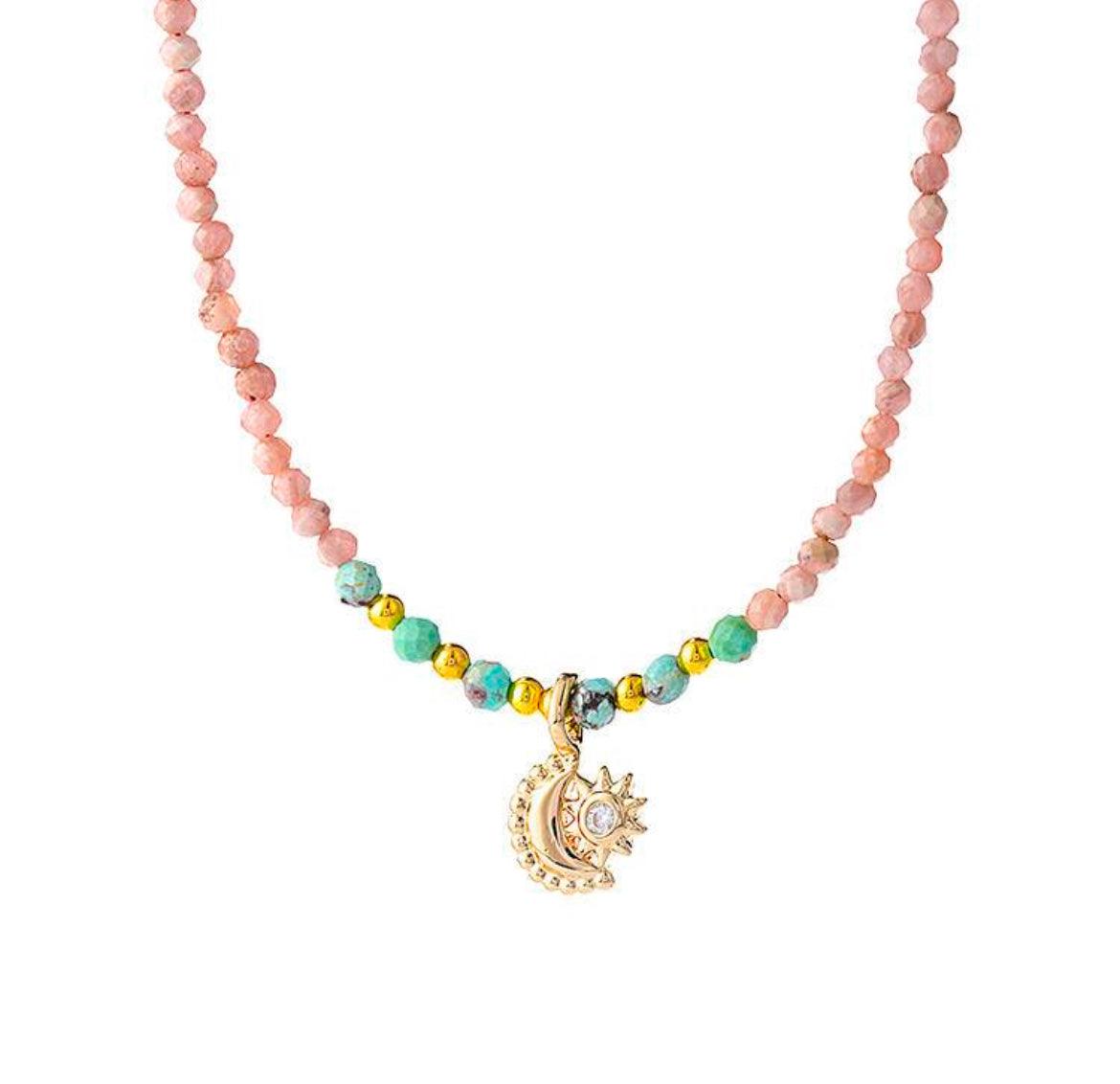 A beaded necklace with pink quartz beads, sun and moon pendant, and diamond details, symbolizing love and good fortune.