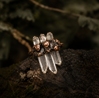 White crystal ring styled on natural stone with earthy moss, copper details, and clear quartz points.