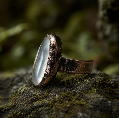 Clear quartz ring with polished translucent stone, organic edges, and dark vintage-toned setting.