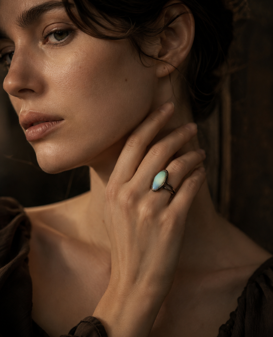 Rainbow moonstone ring styled on the hand with subtle blue-green sheen and quiet feminine mood.