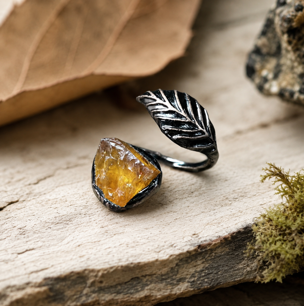 Yellow feather ring displayed on wood and stone with moss, soft shadows, and woodland styling.