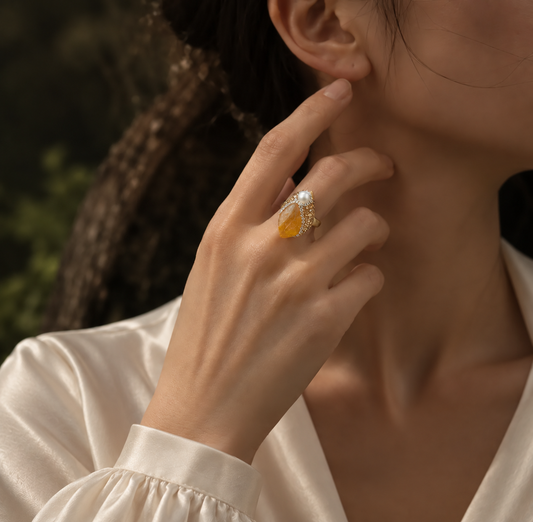 Woman wearing a citrine ring with a honey-yellow stone, pearl accent and teardrop-shaped face in soft forest light