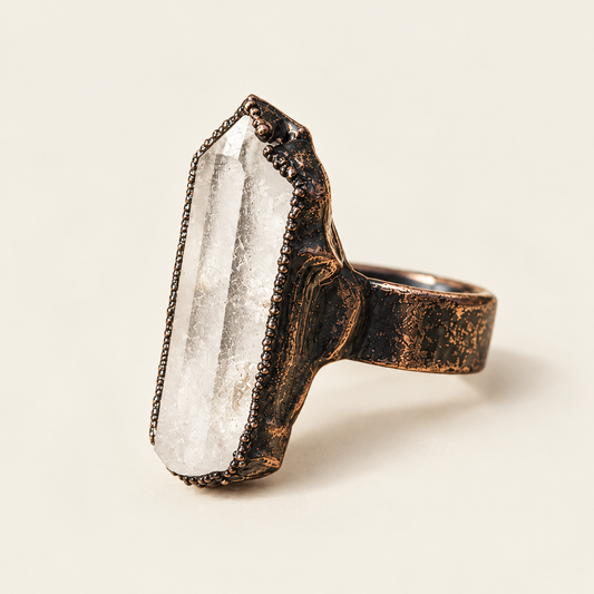Clear quartz crystal ring on warm off-white, showing the tall point, clear stone texture, and full ring profile.