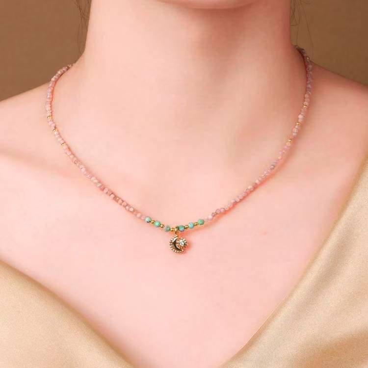 An elegant pendant necklace featuring pink beads, green and yellow accents, and a celestial charm.